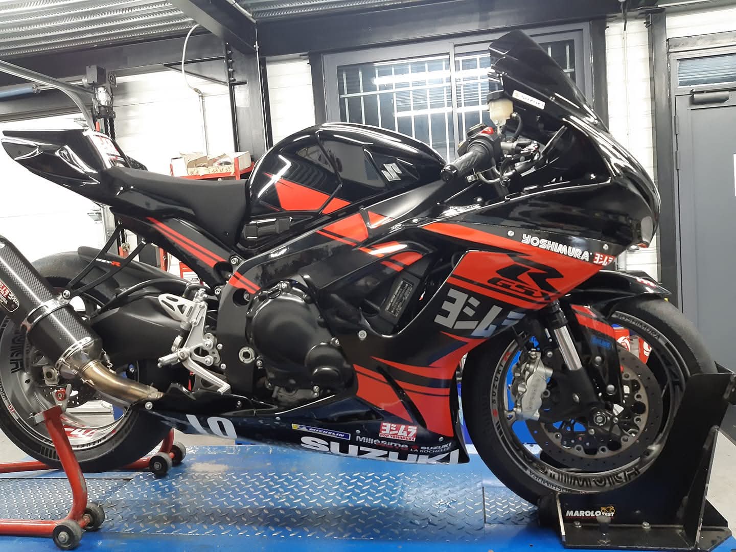 Suzuki GSX-R noire et rouge terminée avec kit déco Yoshimura, prête pour la piste.
