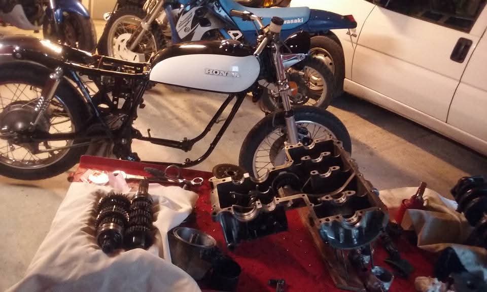 Honda en cours de remontage sur pont élévateur, réservoir blanc repeint et moteur en réfection sur l'établi.