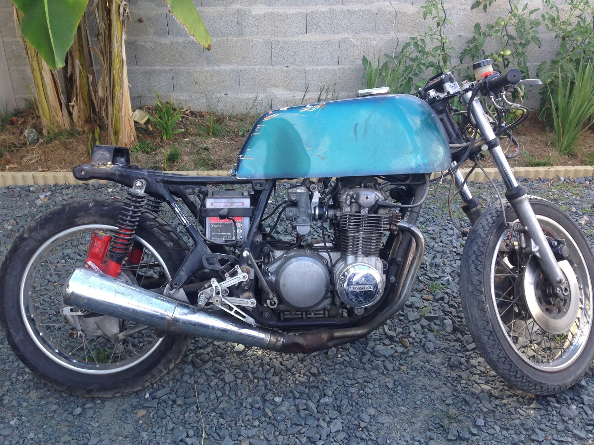 Honda café racer d'origine à l'abandon, réservoir bleu usé et cadre encrassé avant restauration.